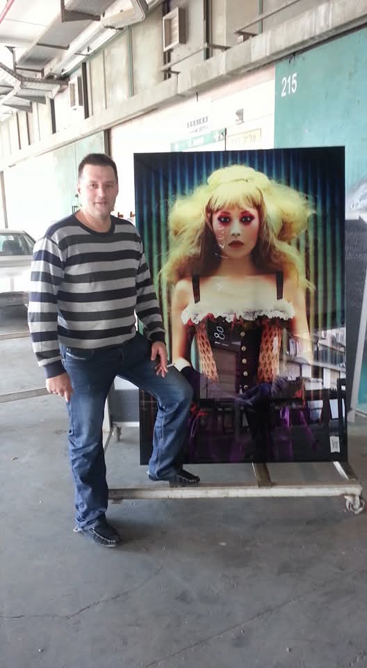 A person stands beside a large portrait panel outside the workshop.